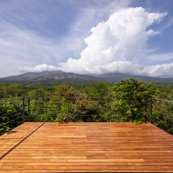 Wooden deck overlooking lush landscape with mountains and cloudy sky.