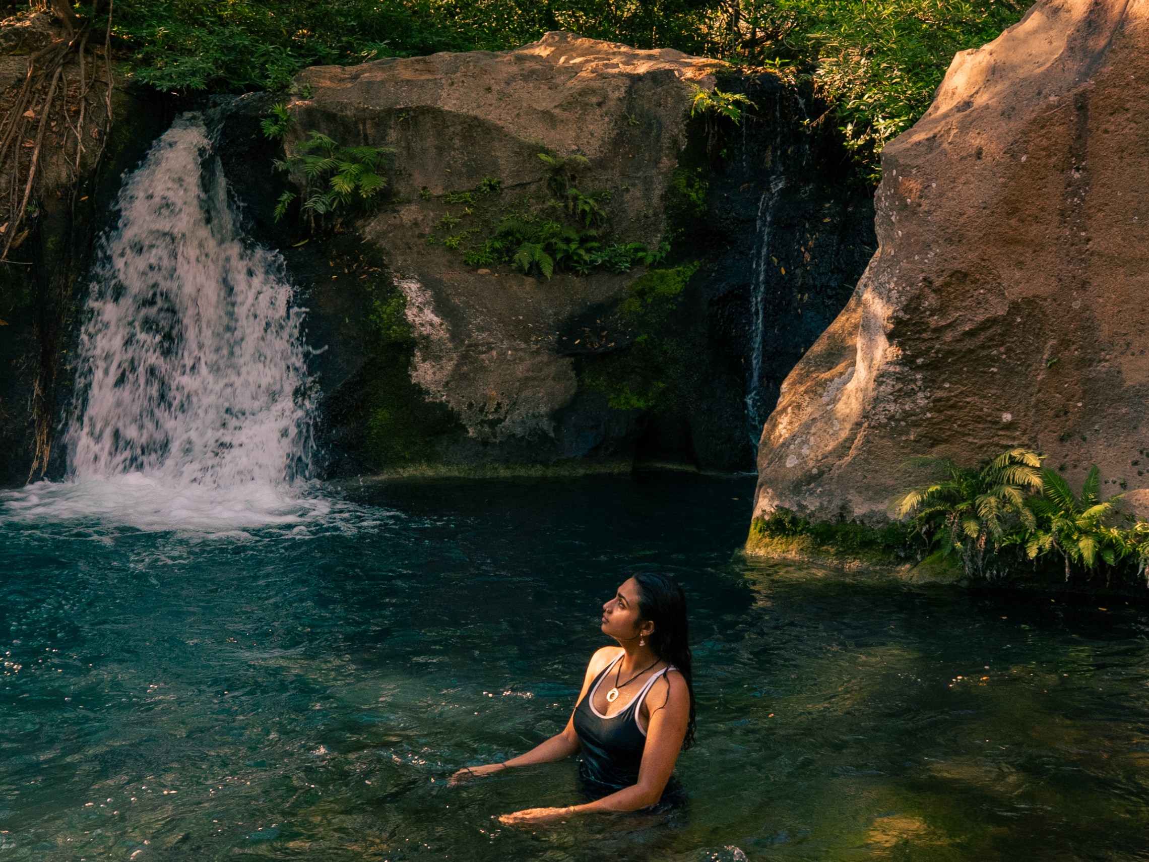 Person swimming in a forest waterfall pool.