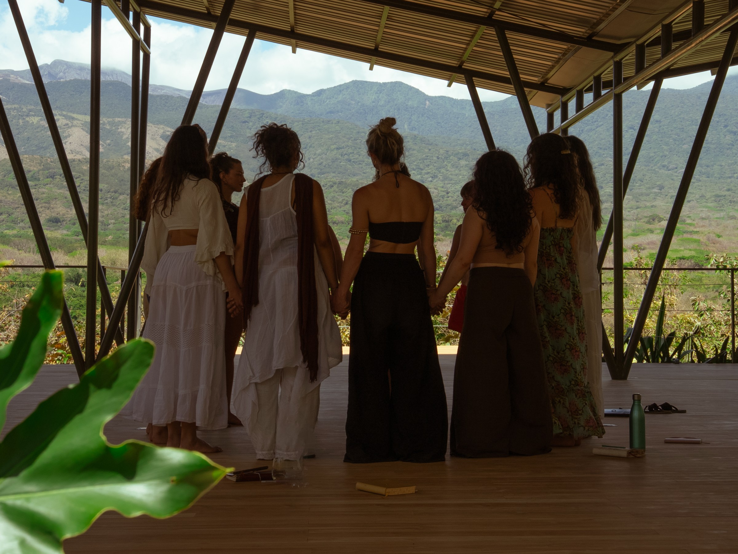 Group of people holding hands in a pavilion with mountains in the background.