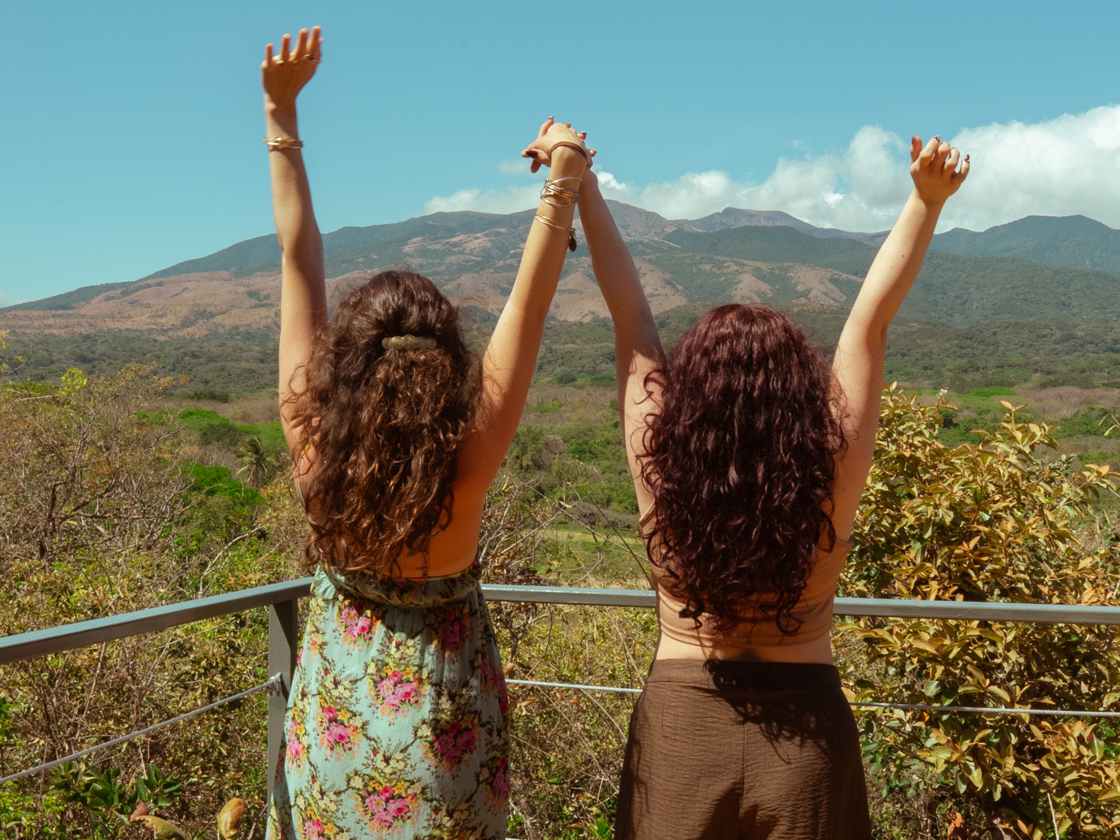 Two people with raised arms facing a mountain view.
