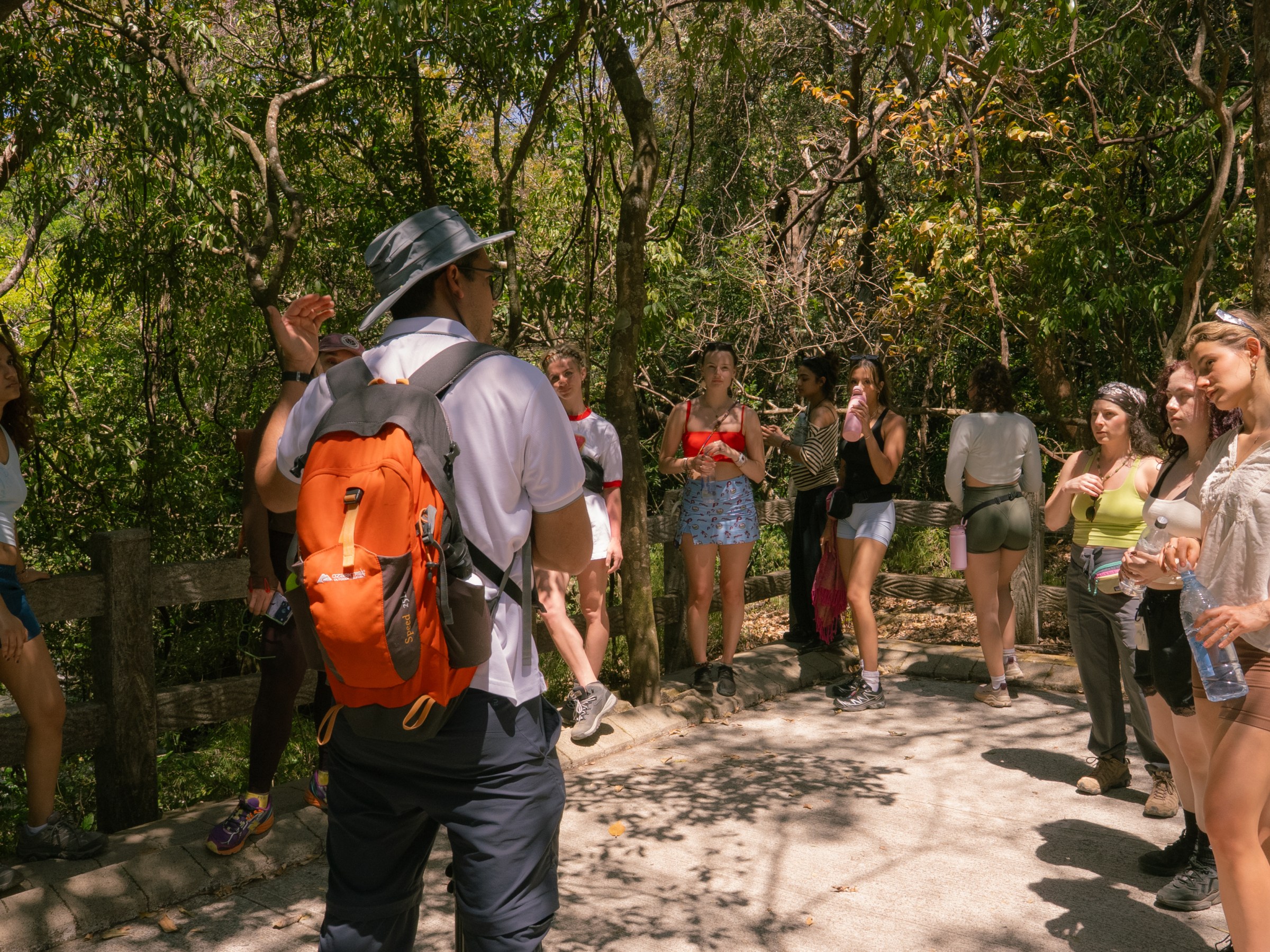 Group of people standing outdoors, some with backpacks, in a forested area.