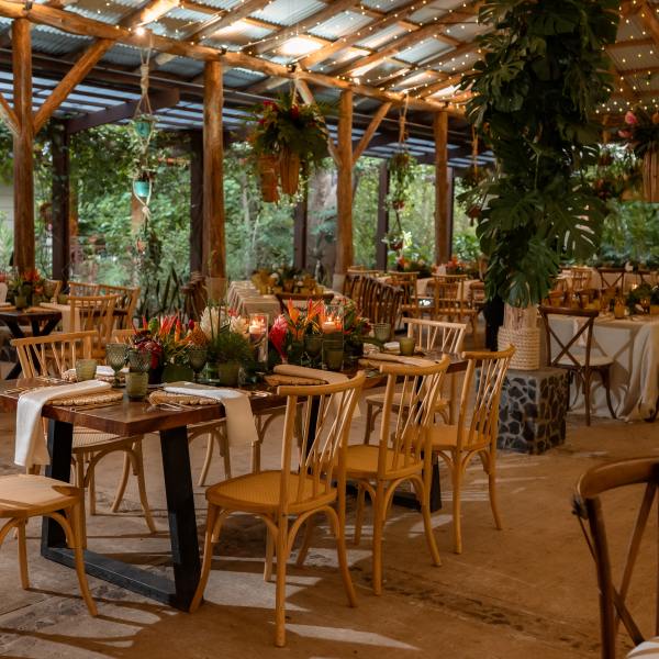 Rustic event venue with wooden tables, chairs, and greenery under string lights.