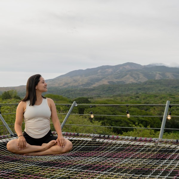 Woman sitting on net platform with mountain view in the background.