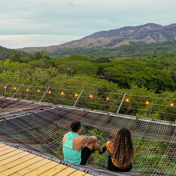 People sitting on a net with a scenic view of mountains and forest.