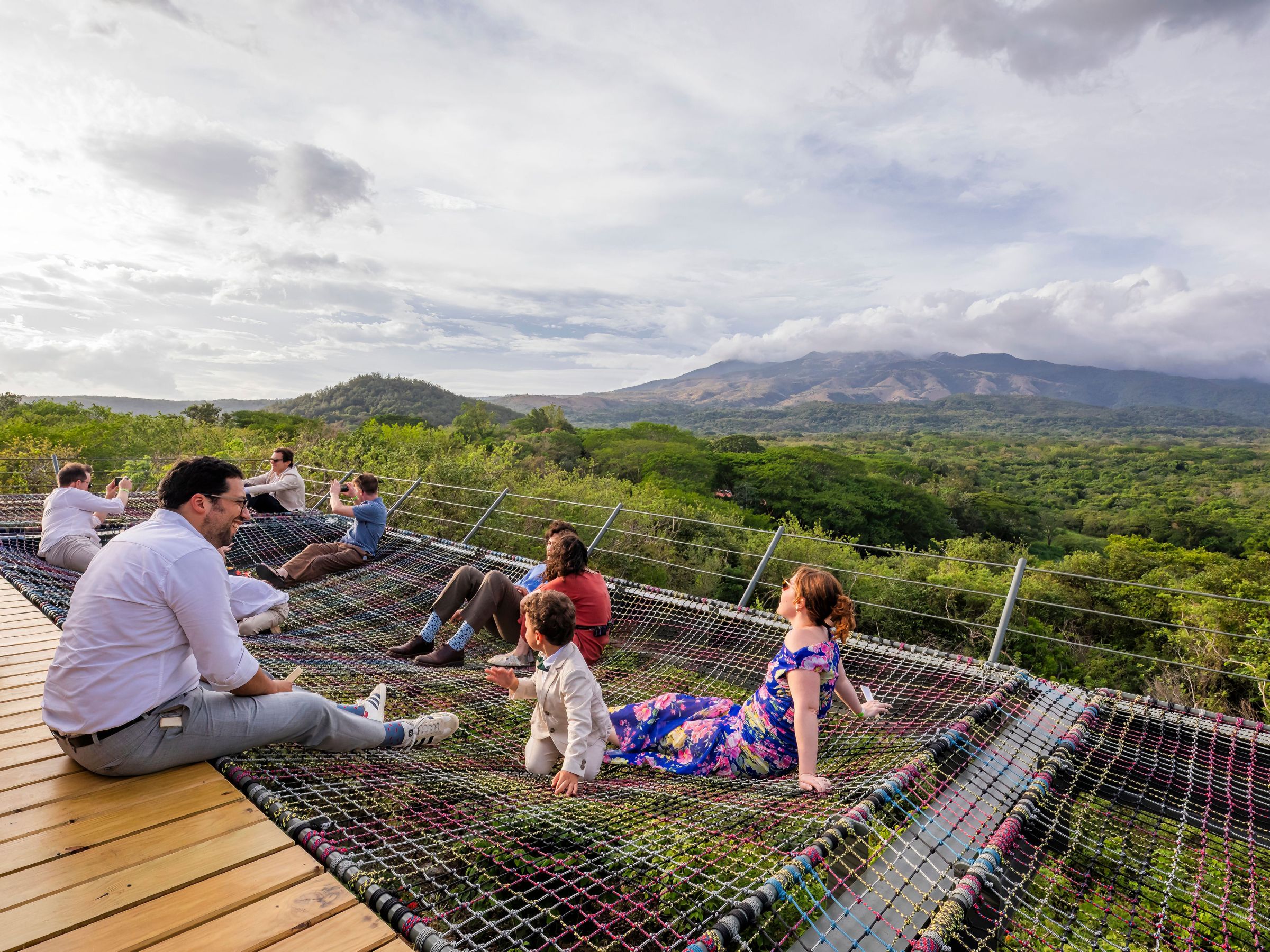 People relaxing on net hammocks overlooking a lush landscape and distant hills.