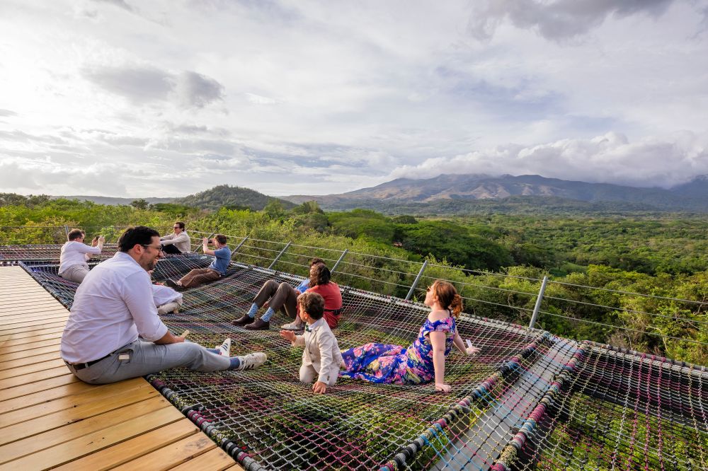 People relaxing on net hammocks overlooking a lush landscape and distant hills.