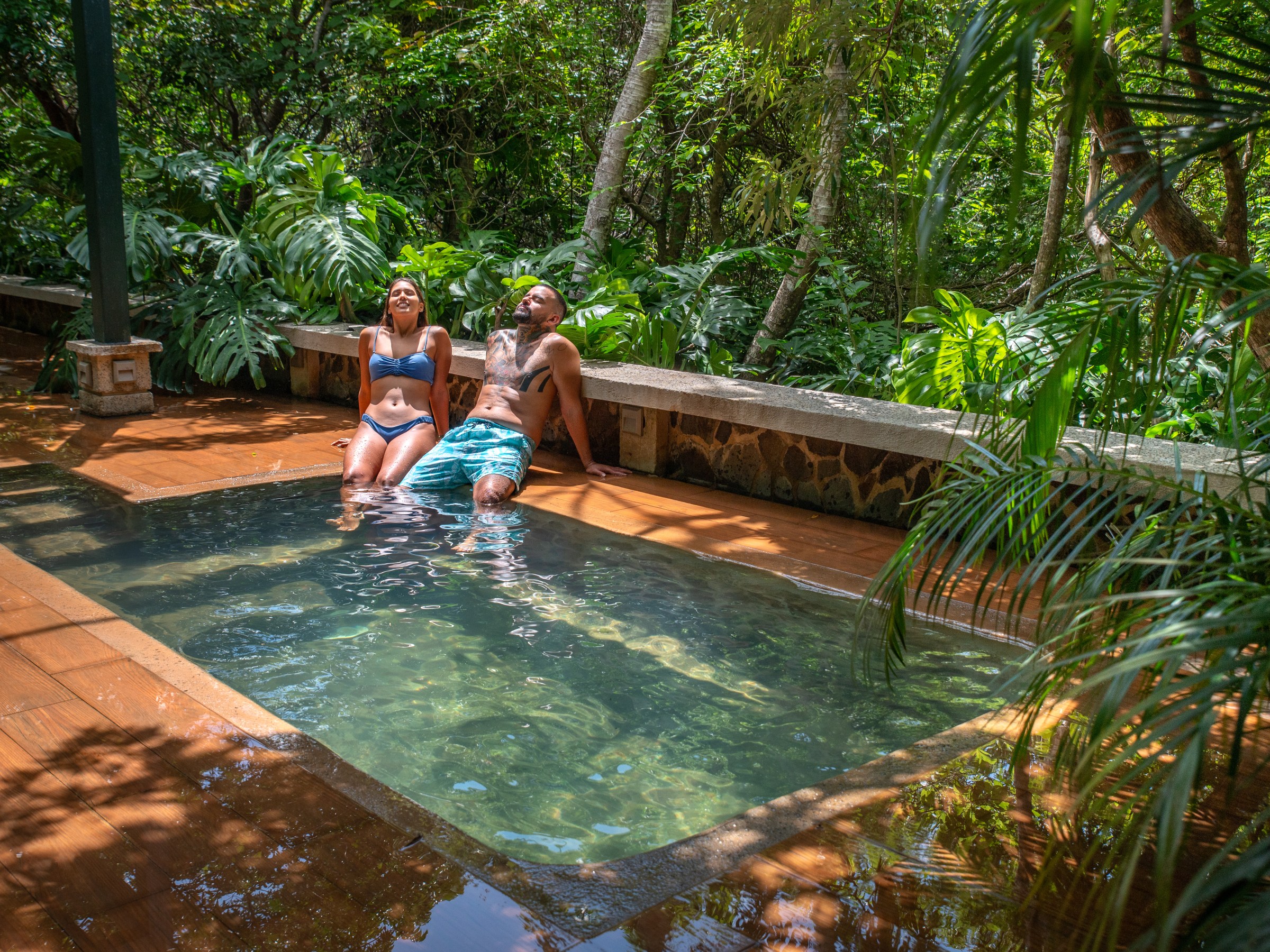 Two people relaxing in a small pool surrounded by lush greenery.