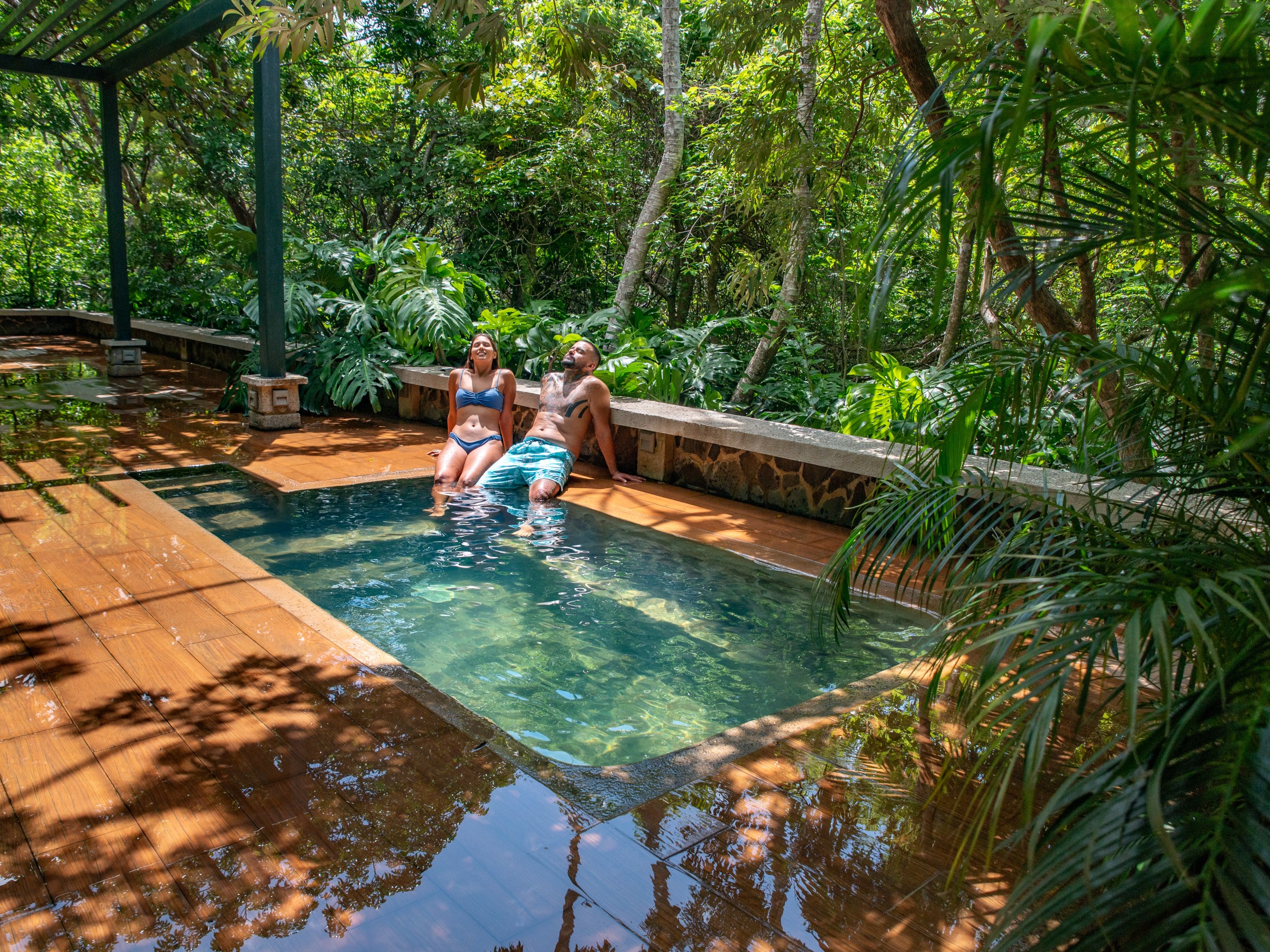 Two people sitting by a small pool in a lush, tropical setting.