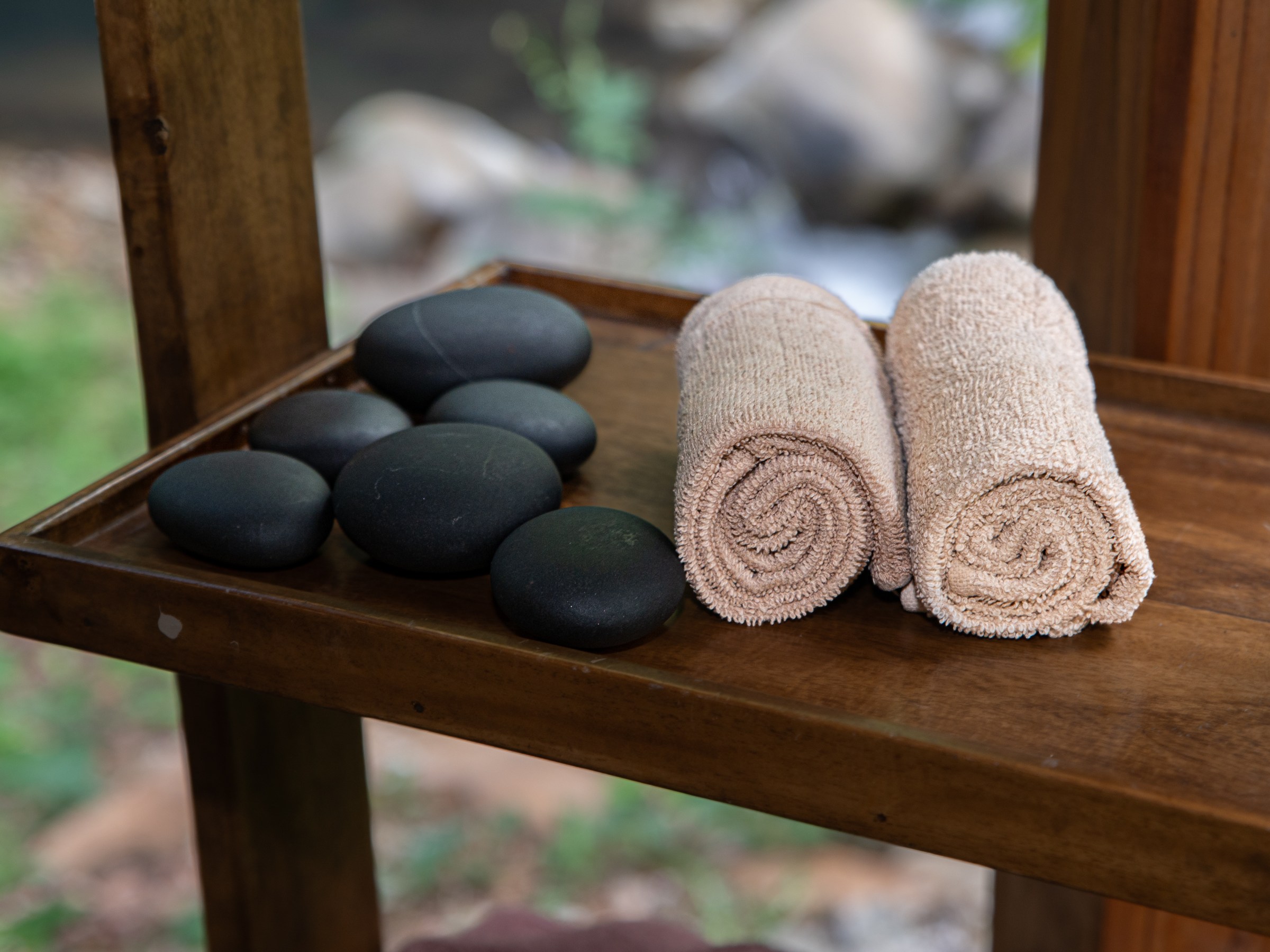 Two rolled towels and smooth black stones on a wooden shelf.