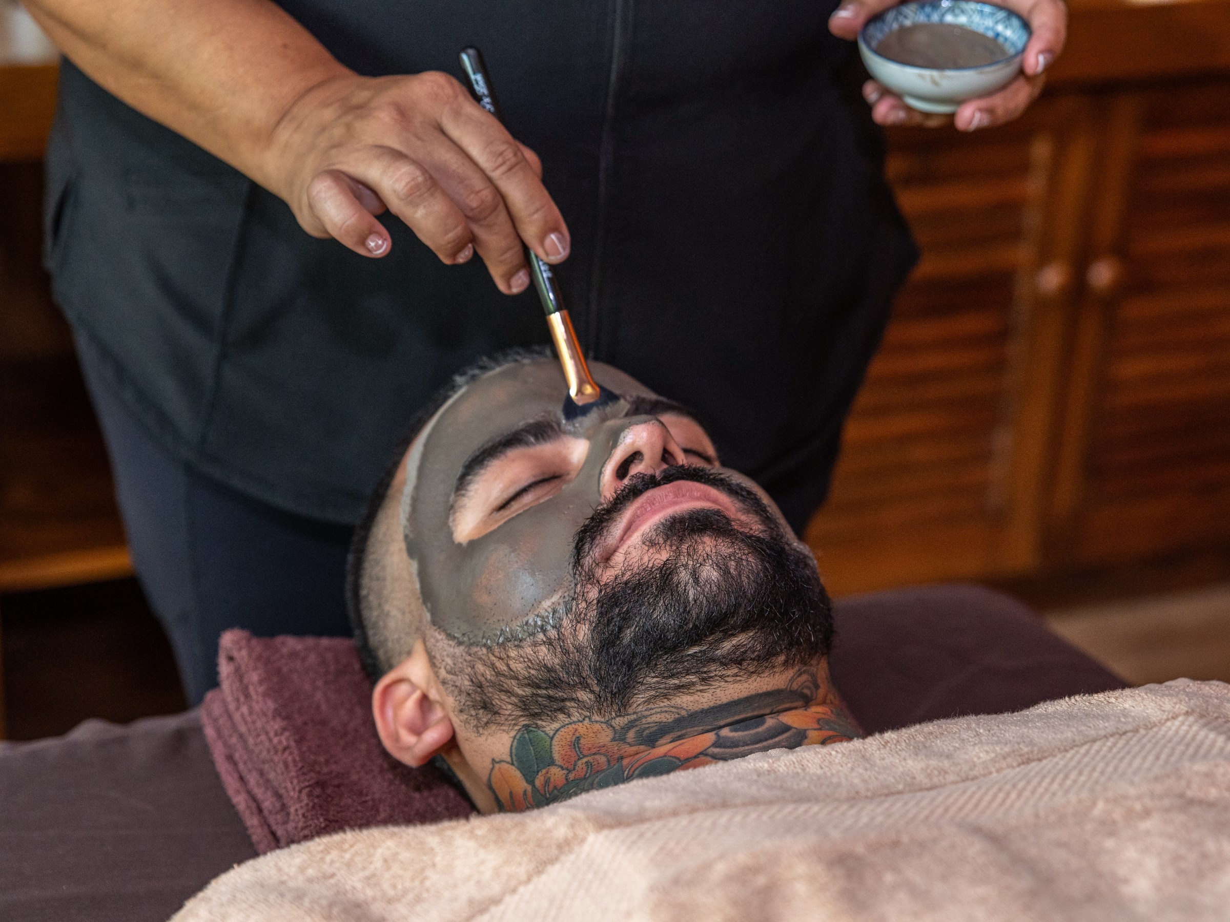 Person receiving a facial treatment with a black mask applied to their face.