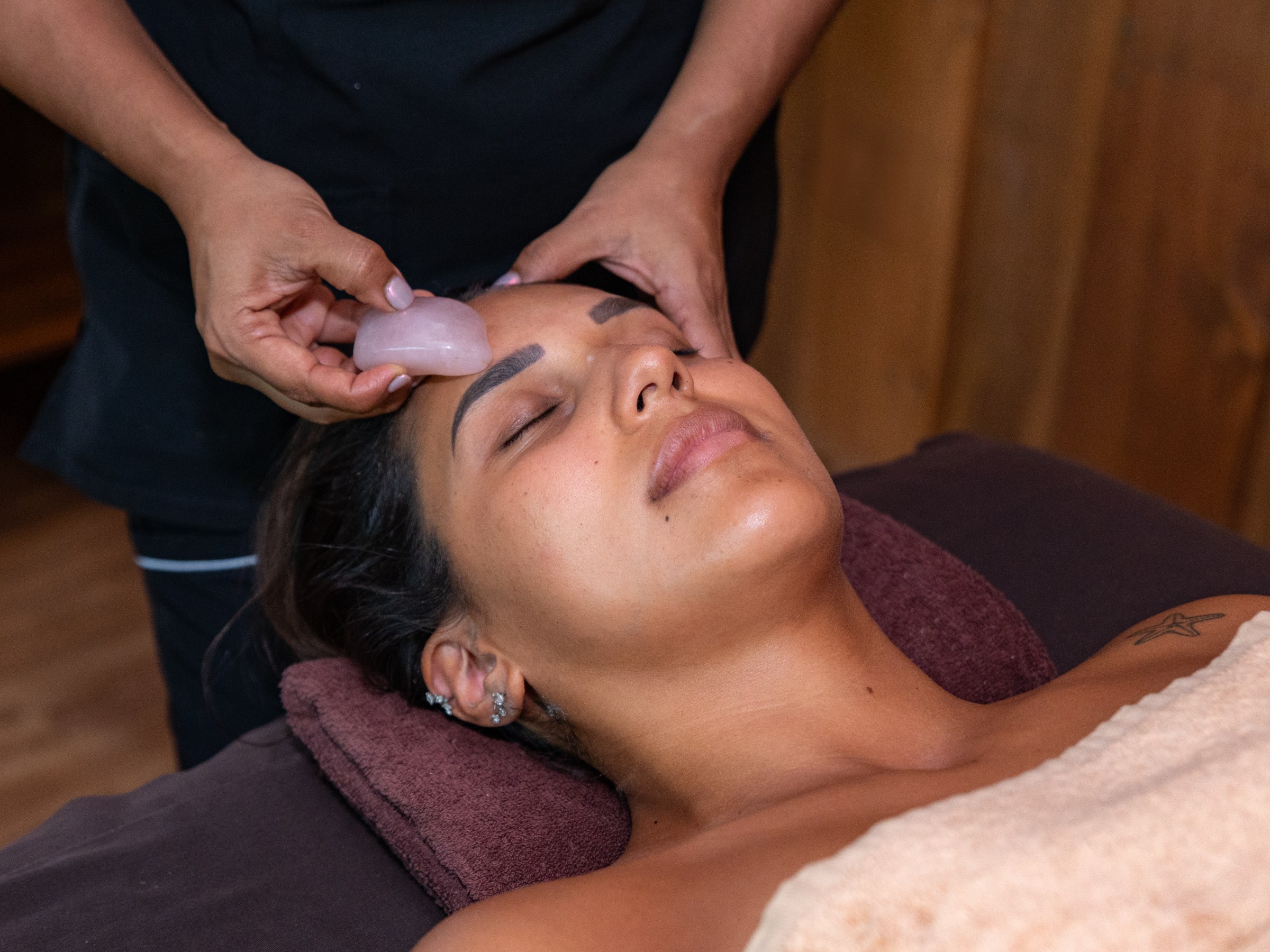 Person receiving a facial massage with a pink stone roller.