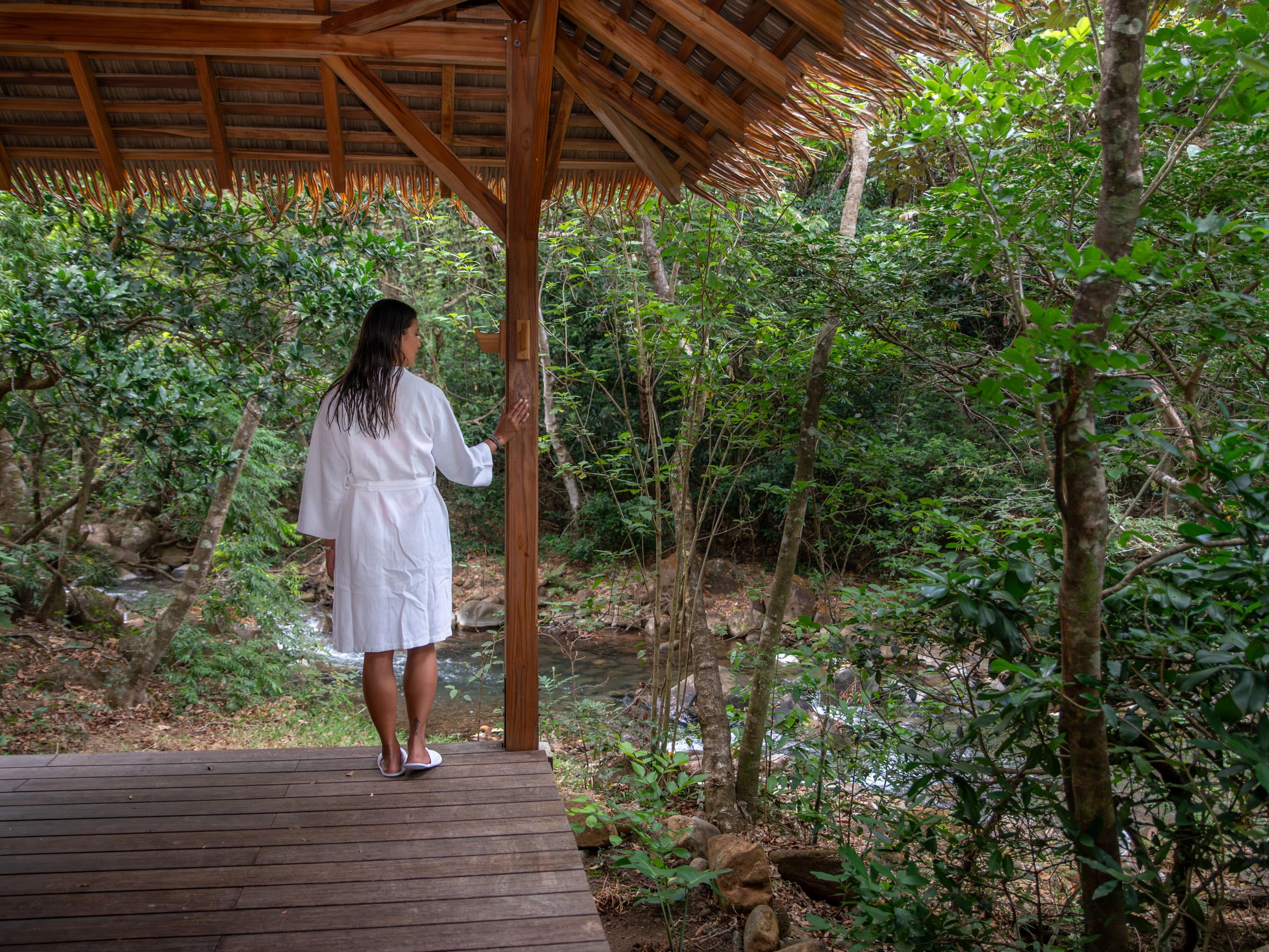 Person in a robe stands on a wooden deck overlooking a forest.