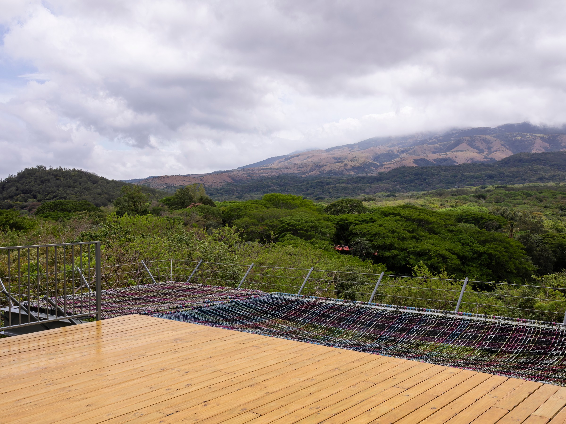 Wooden deck overlooking lush landscape and distant mountains under cloudy sky.