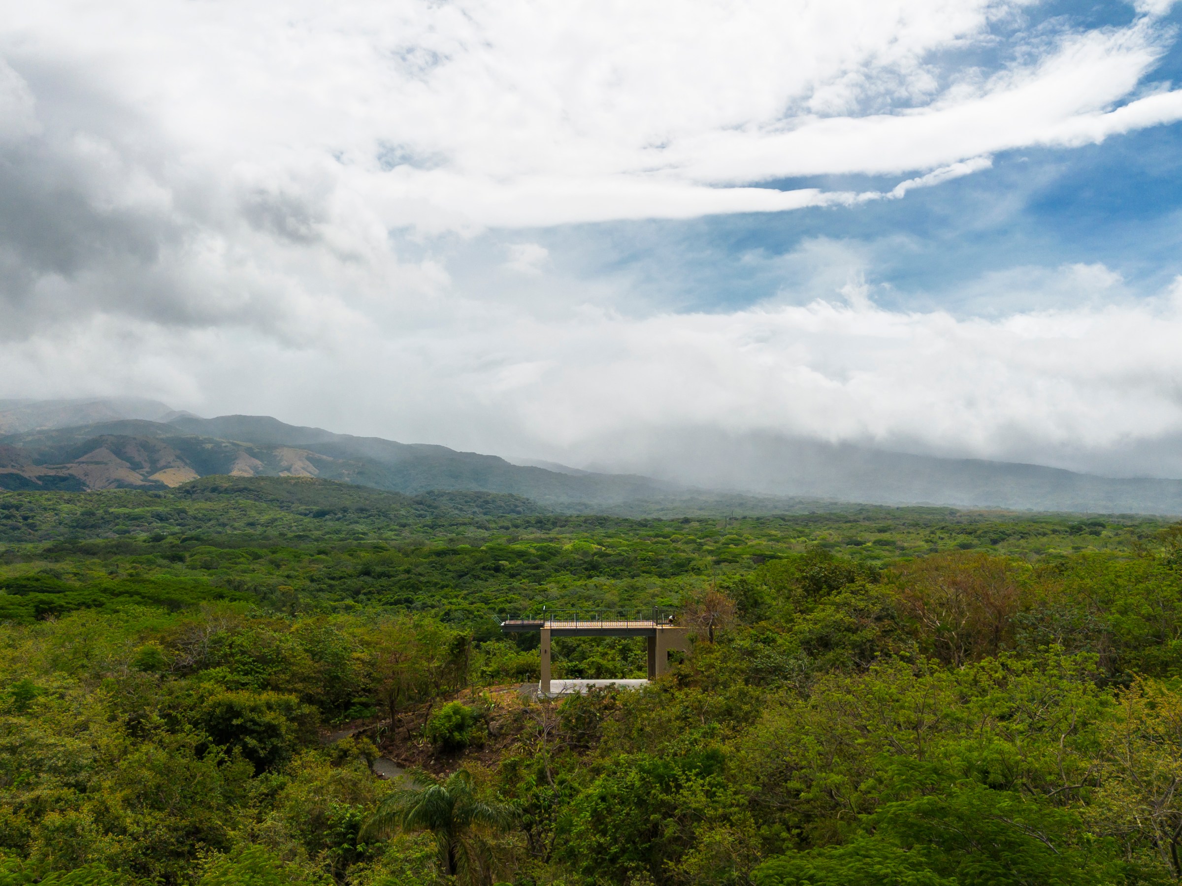 Cloudy sky over a vast green landscape with mountains in the background.