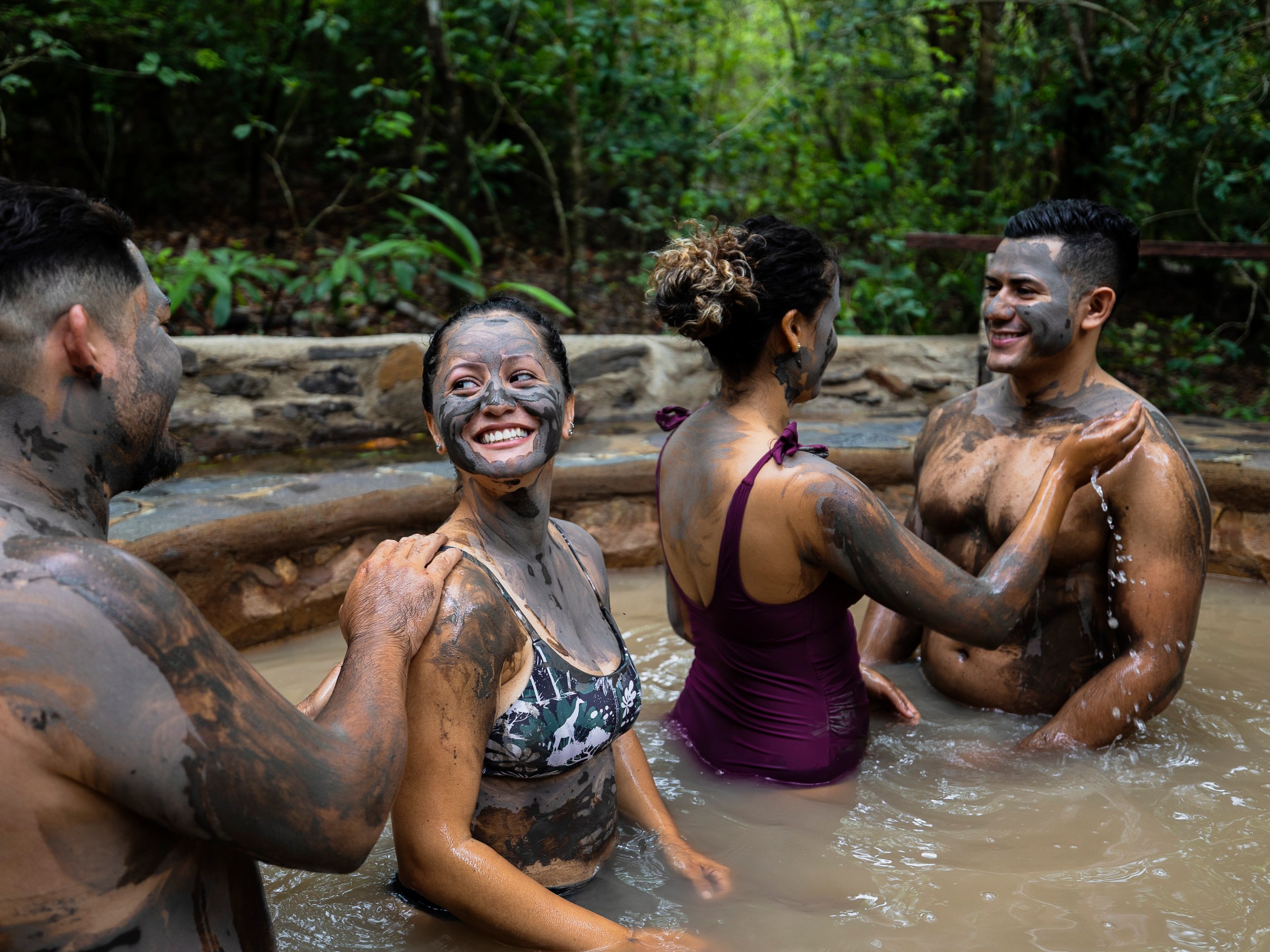 Four people with mud face masks enjoying a hot spring.