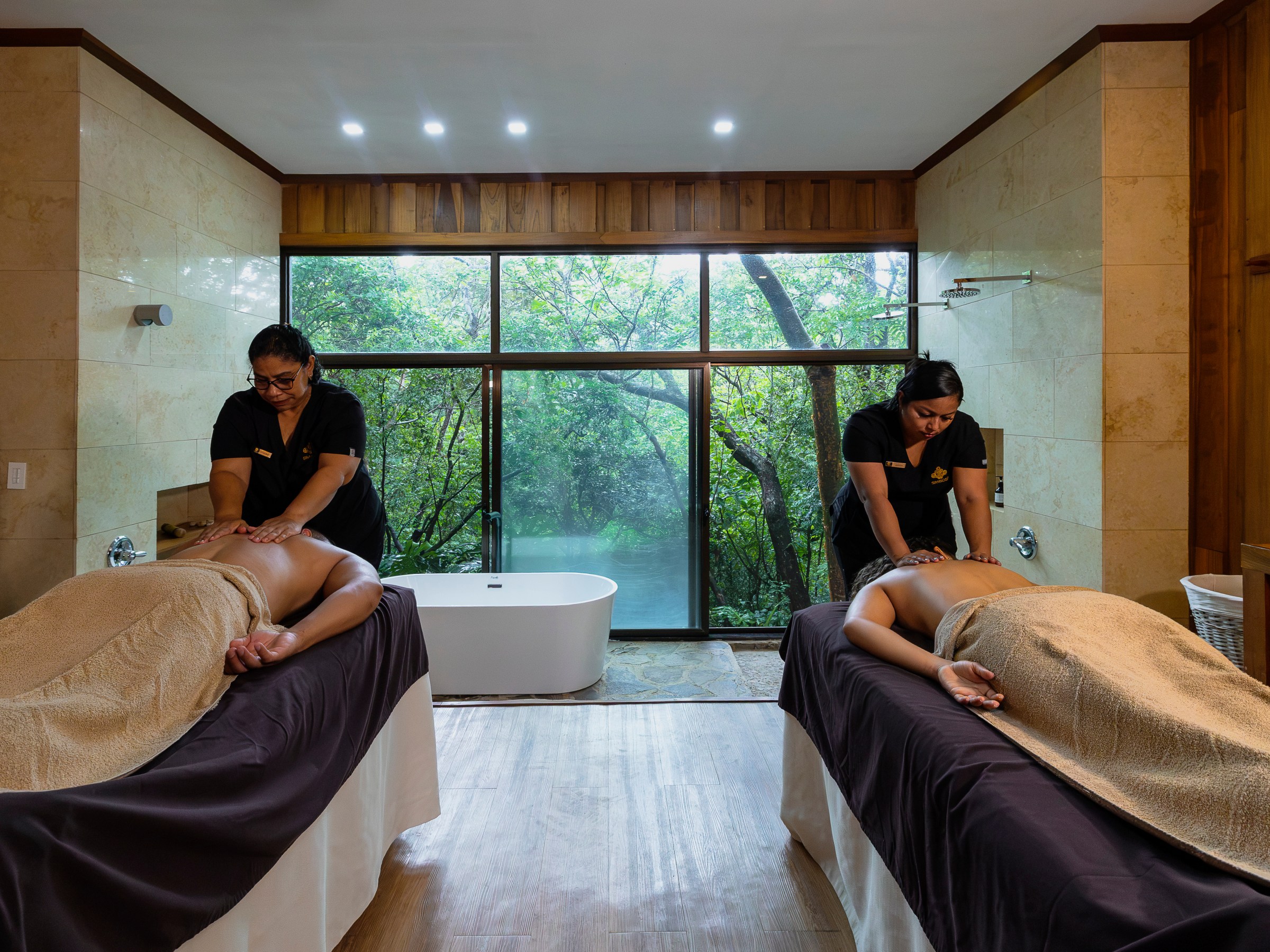Two people receiving massages in a spa room with large window view.