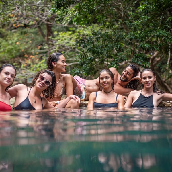 Group of people smiling and relaxing in a natural body of water with trees in the background.